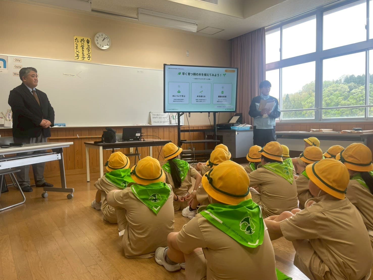 教室で「早く育つ桐の木を植えてみよう！」のスライドを前に、講師の説明を聞く児童たち